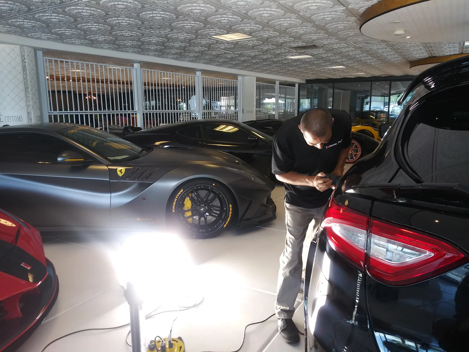 Technician working on a black exotic sports car under detailing lights